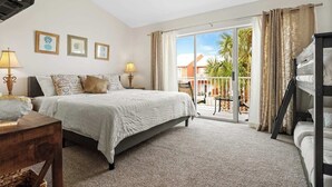 A bedroom with a bed, two bedside tables with lamps, a ceiling fan, a window with curtains, and a balcony with a table and chairs. - Location, location, location! Steps to the pool and just a 5-minute walk to the beach 🏖️💦 (Miramar Beach)
