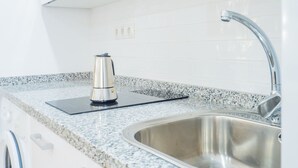 A kitchen with a stainless steel sink, a kettle on a black mat, and a microwave above the counter. - Cubo's Urban Studio Turisbelen / city / free wifi (Málaga)