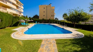 A swimming pool surrounded by a stone pathway, with lounge chairs and a tall building in the background. - Cubo's Luna Beach Mijas Costa / Close to the beach / free wifi (Mijas Costa)