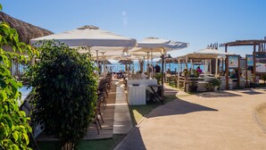 An outdoor seating area with umbrellas, wooden tables, and chairs, overlooking a body of water. - Cubo's Luna Beach Mijas Costa / Close to the beach / free wifi (Mijas Costa)