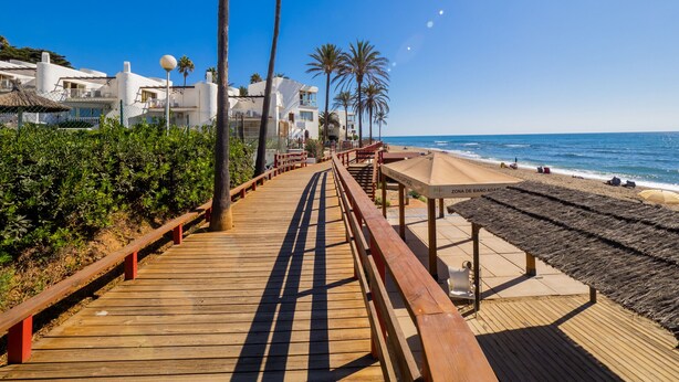 A wooden boardwalk leading to a beach with palm trees and white buildings. - Cubo's Luna Beach Mijas Costa / Close to the beach / free wifi (Mijas Costa)