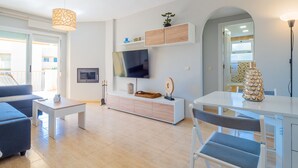 A modern living room with a sofa, coffee table, TV, and a dining area with chairs. - Cubo's Luna Beach Mijas Costa / Close to the beach / free wifi (Mijas Costa)