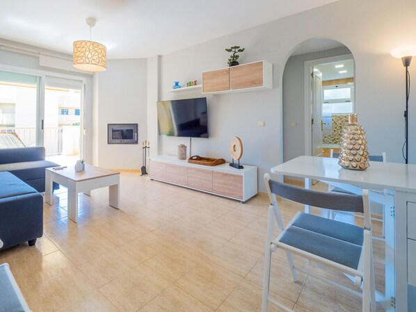 A modern living room with a sofa, coffee table, TV, and a dining area with chairs.