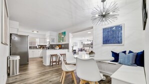 A modern kitchen with white cabinetry, a stainless steel refrigerator, and a dining area with white chairs and a white table. - Best Little Bunkhouse in TX! Walk to FIFA WORLD CUP (Arlington)
