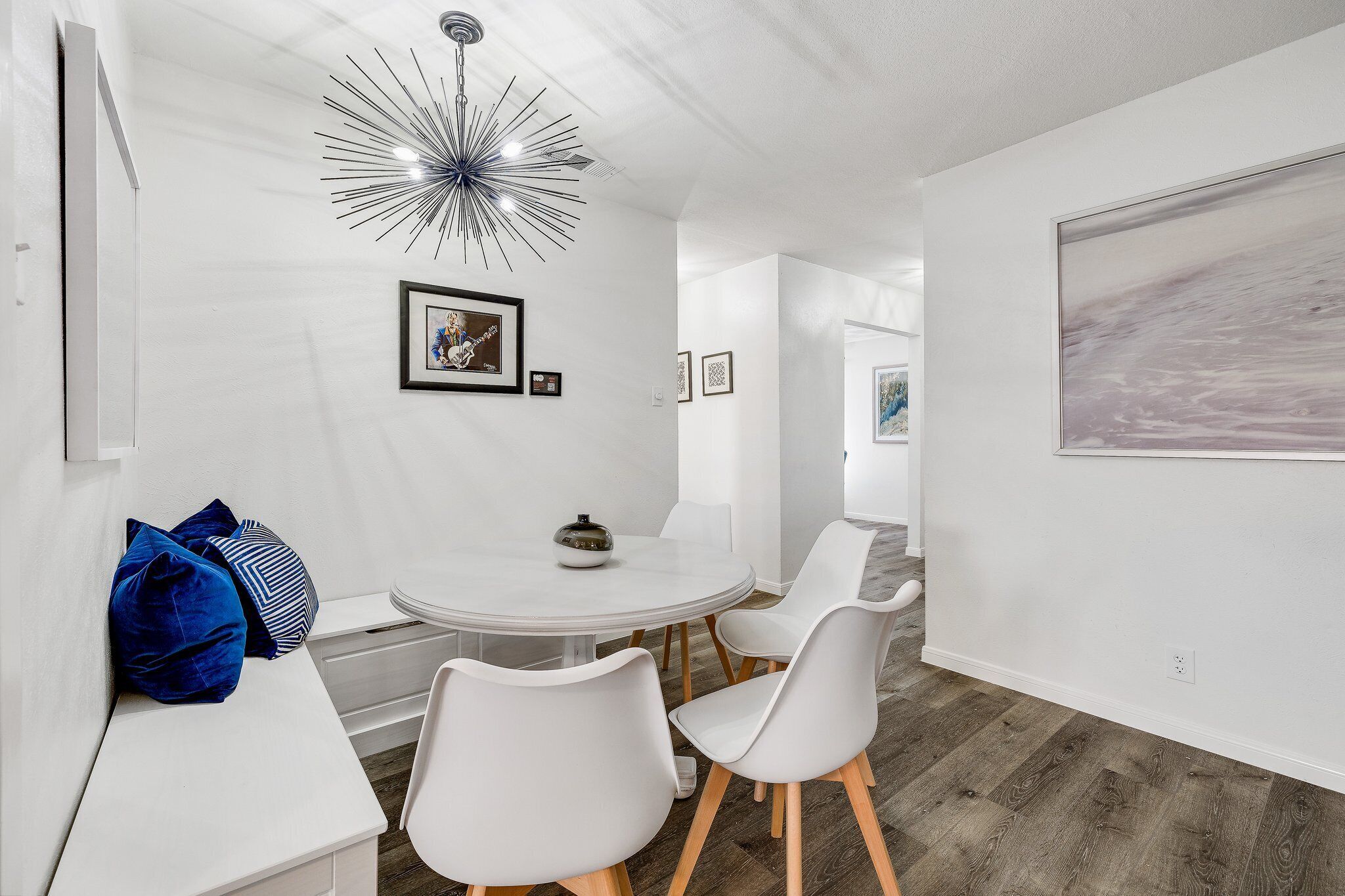 A modern dining area with a round table, white chairs, and a unique ceiling light.
