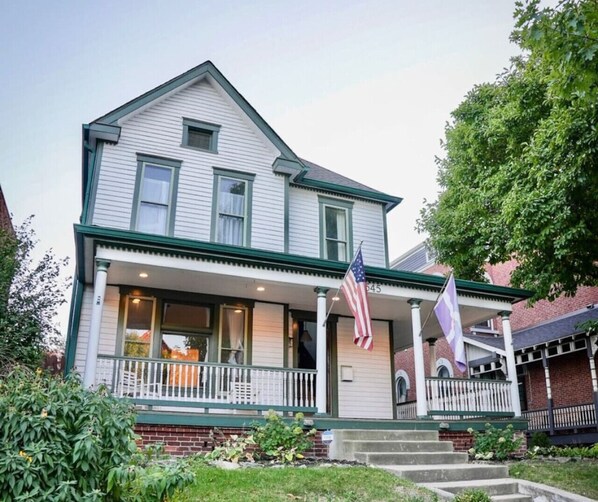 A two-story house with a porch, an American flag, and a flag with a purple symbol.