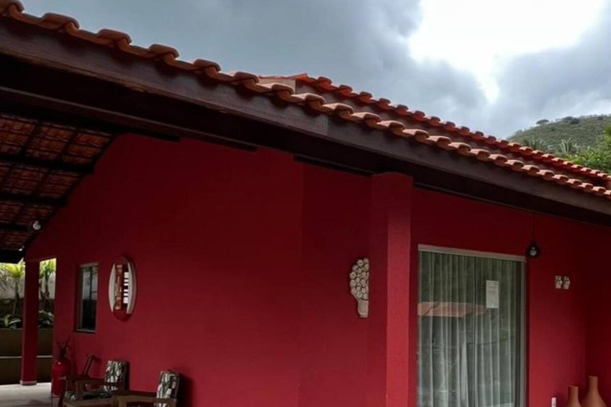A red building with a tiled roof, a covered patio with chairs, and a glass door.