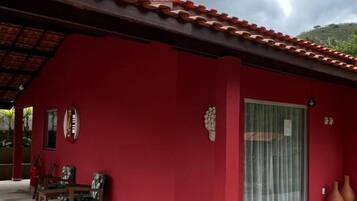 A red building with a tiled roof, a covered patio with chairs, and a glass door.