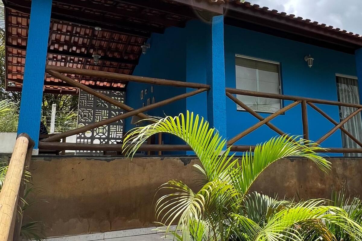 A blue building with a tiled roof, a wooden fence, and a palm tree in the foreground.