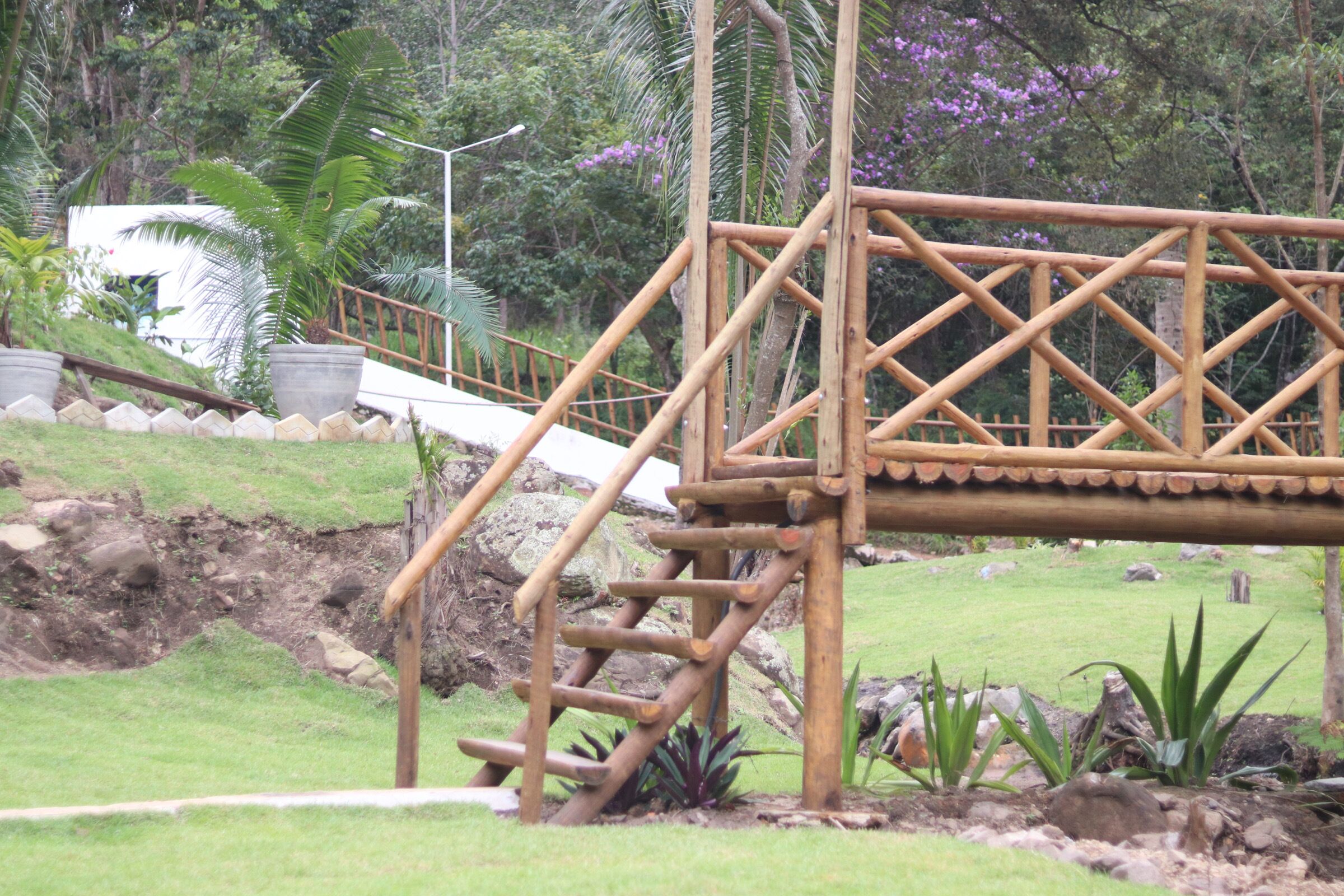 Un puente de madera con una escalera que conduce hacia él, rodeado de follaje y rocas.