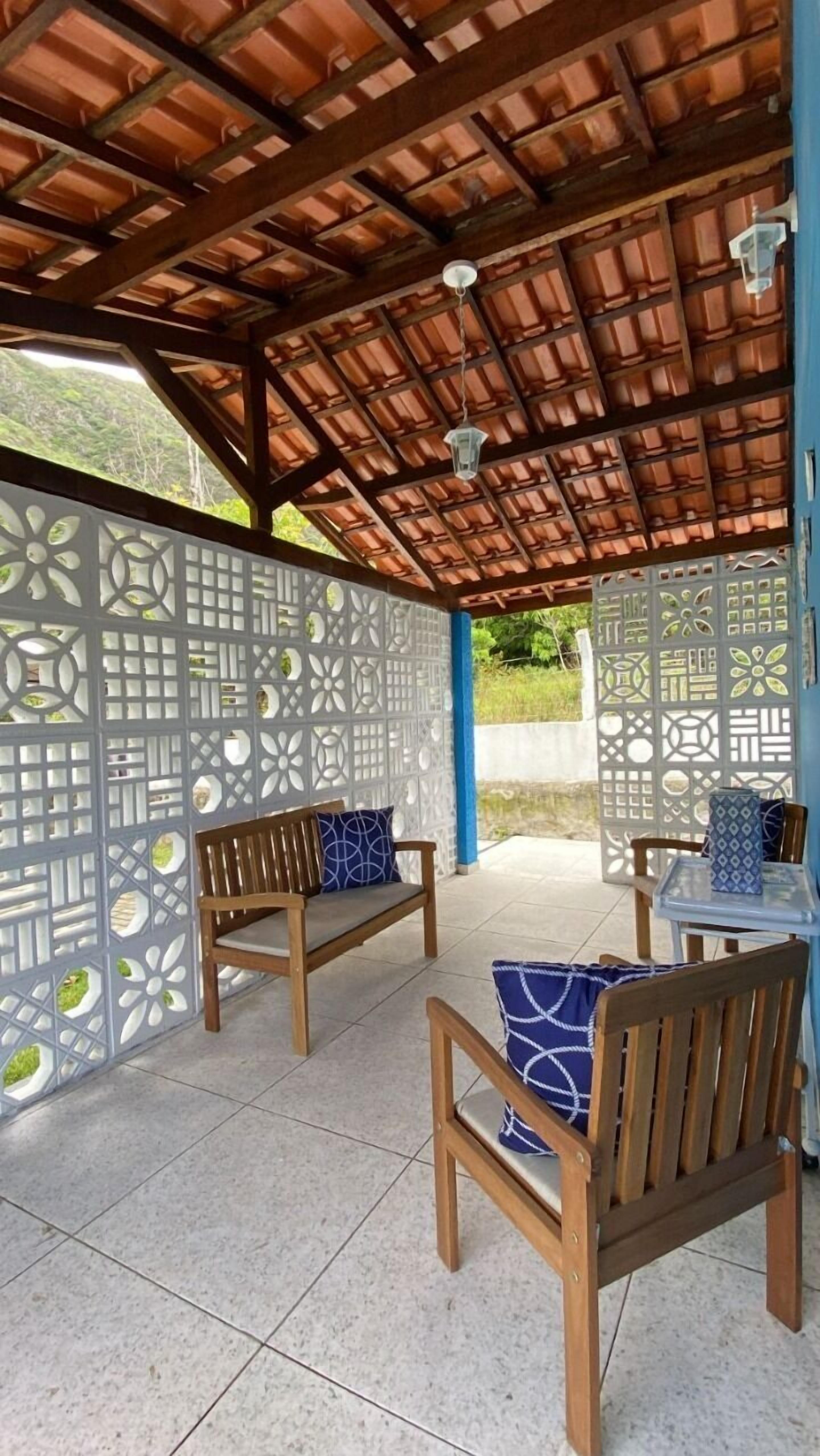An outdoor seating area with wooden benches and chairs, a tiled floor, and a decorative partition with geometric patterns.