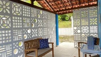 An outdoor seating area with wooden benches and chairs, a tiled floor, and a decorative partition with geometric patterns.