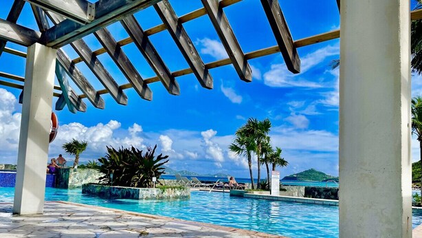 Ein Poolbereich mit klarem, blauem Wasser, einer Pergola und Palmen.