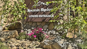 Un panneau indiquant l’entrée inférieure de Mountain Shadow, entouré d’un mur de pierres et de verdure.