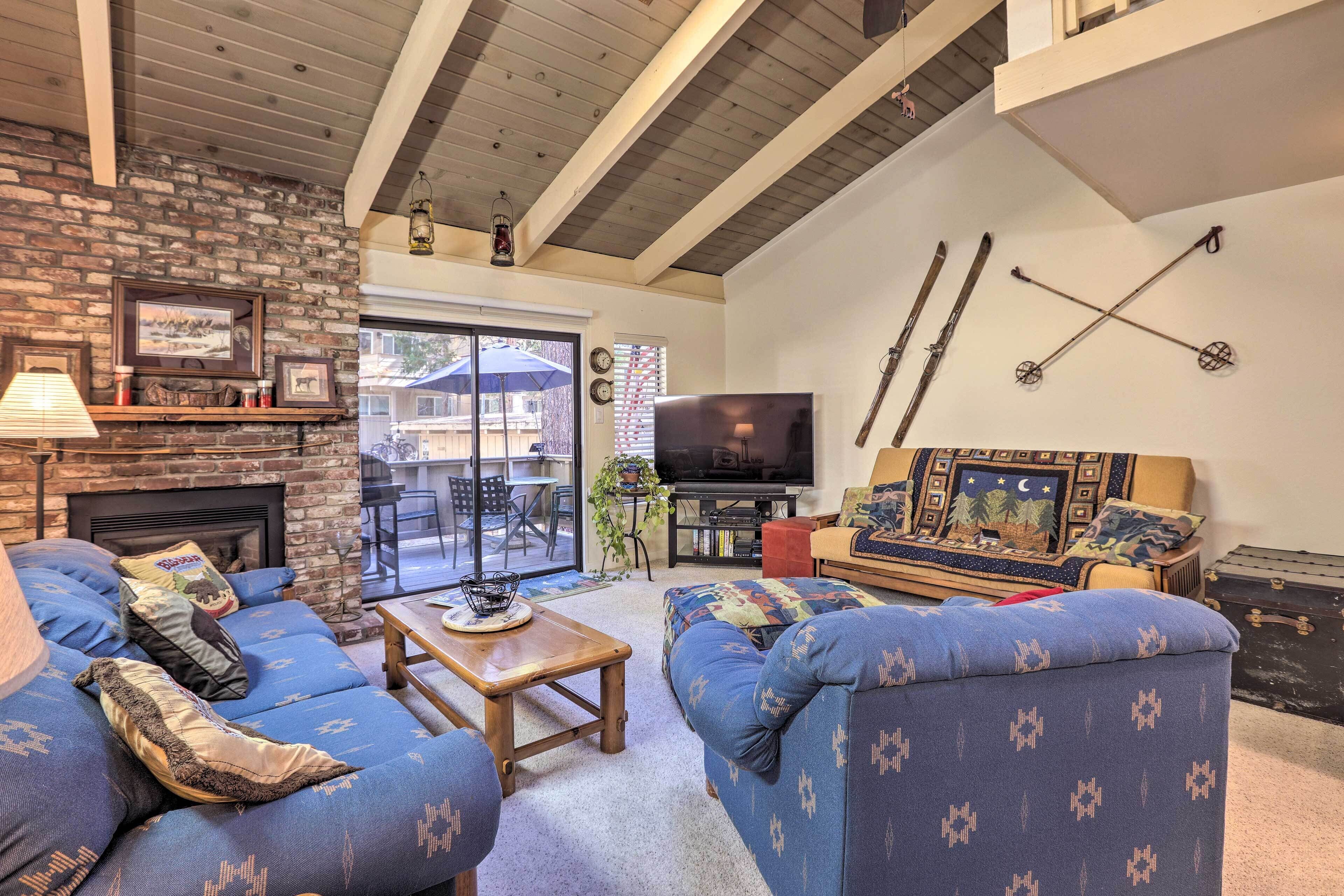 A cozy living room with a fireplace, blue patterned sofas, a TV, and ski equipment on the wall.
