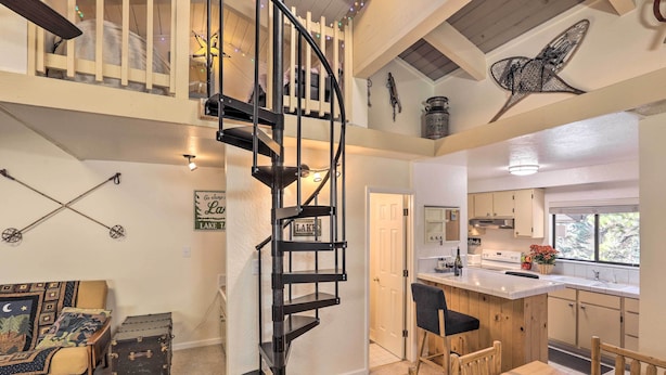 Une cuisine spacieuse avec un îlot central, un coin repas avec des chaises en bois, un escalier en colimaçon et une chambre en mezzanine équipée d’un lit superposé.