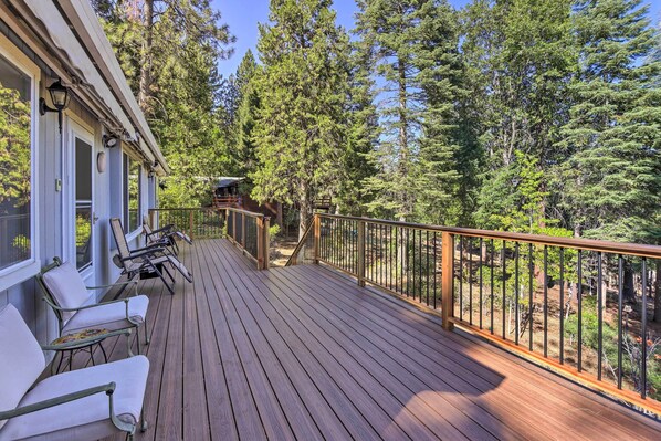 Terraza de madera con mobiliario exterior y vista a un bosque.