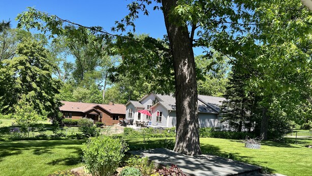 A residential area with a large tree, a wooden deck, and two houses with different roofing styles. - Beautifully styled, Mid Century Modern, family friendly Lake Mills House! (Lake Mills)