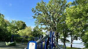 A playground with slides and swings, surrounded by trees and a body of water. - Beautifully styled, Mid Century Modern, family friendly Lake Mills House! (Lake Mills)