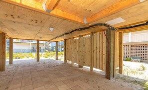 Une terrasse en bois ouverte, avec un sol sablonneux, entourée d’une clôture en bois et offrant une vue sur un quartier résidentiel.