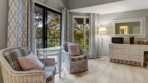 Een kamer met rieten meubels, een glazen tafel, een kast en een groot raam met gordijnen.