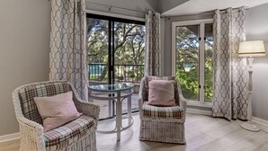 Een balkon met rieten stoelen, een glazen tafel en gordijnen.