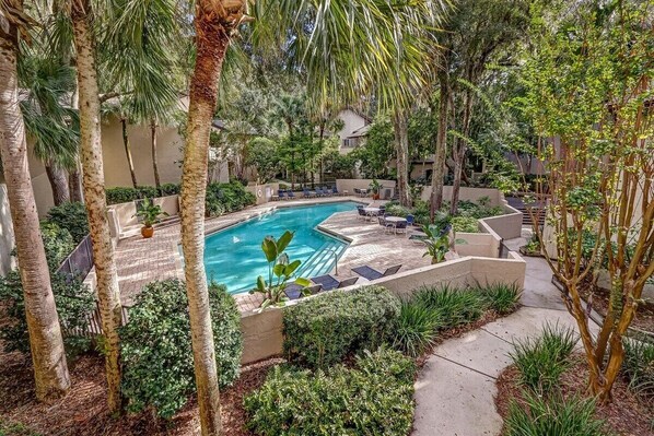 Relax by the serene pool surrounded by lush greenery and palm trees.