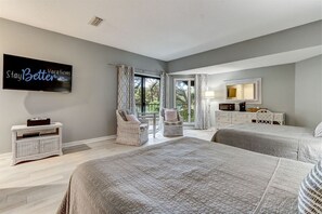 Two large beds with matching bedding, a wicker chair, and a side table are featured in this inviting bedroom.