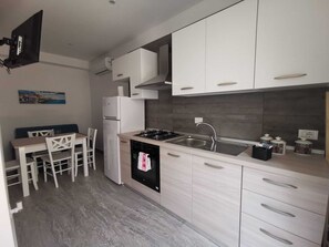 Una cucina moderna con mobili bianchi, piano cottura a gas, lavello e zona pranzo con tavolo e sedie.
