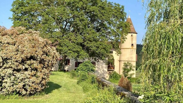 A historic building with a tower, surrounded by lush greenery and a well-maintained lawn.