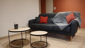 A modern living room with a dark grey sofa, two round tables, and a red and grey blanket.
