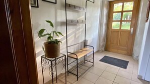 A hallway with a wooden door, a metal rack with hooks, a potted plant, and a tiled floor.