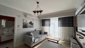 Uma sala de estar moderna com um sofá cinzento, uma mesa pequena e um candeeiro de teto.