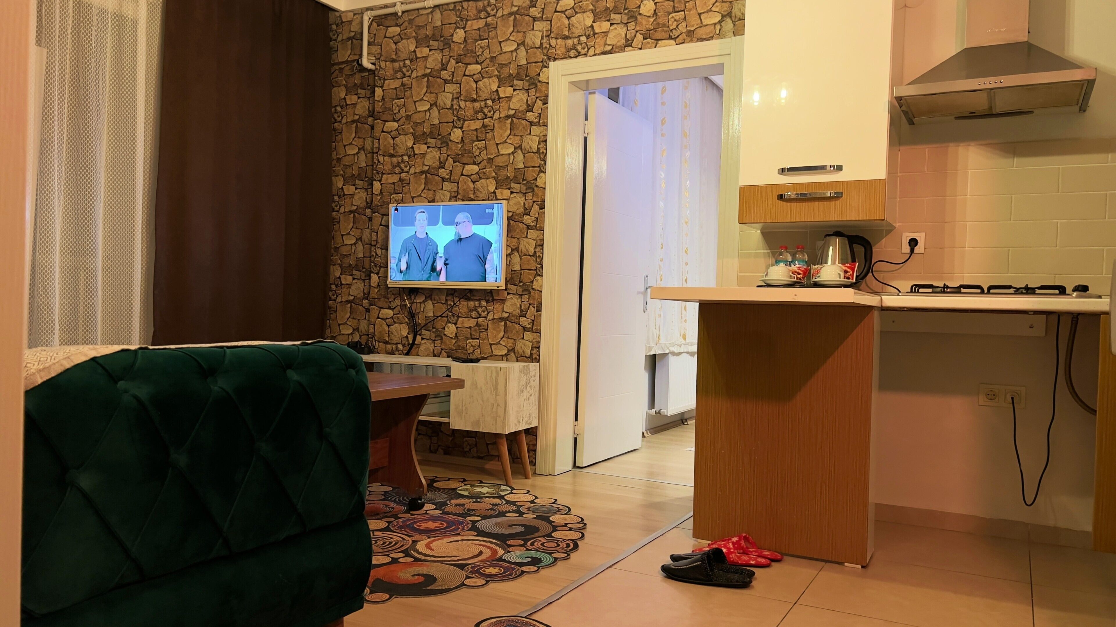 Una sala de estar acogedora con un sofá verde, un tapete estampado y un televisor montado en una pared de piedra.