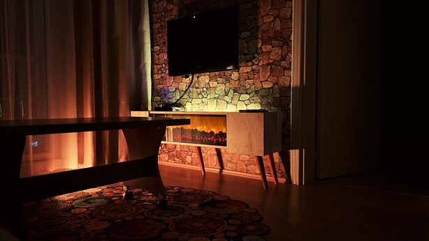 Uma sala de estar acolhedora com lareira, televisão de tela plana fixada em uma parede de pedra e um tapete estampado no chão.