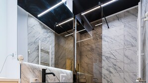 A modern bathroom with a marble floor, a wooden vanity, a black sink, and a glass shower enclosure.