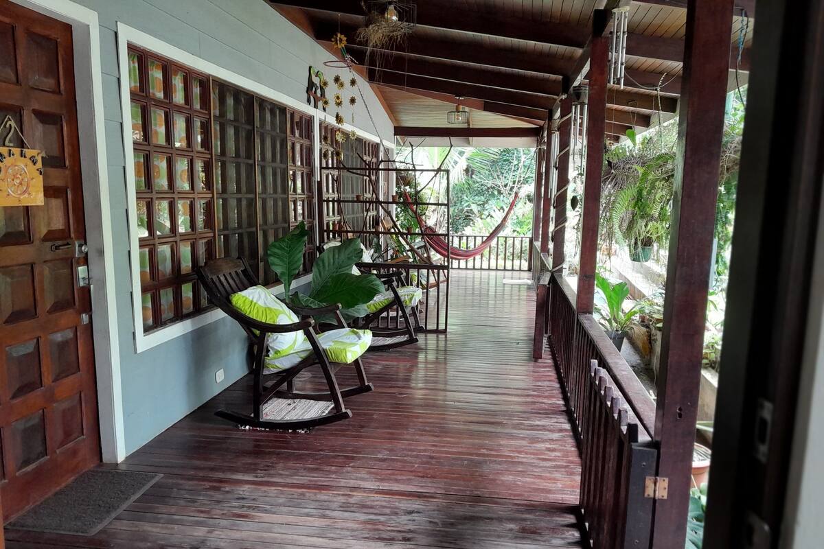 Un porche de madera con mecedoras y una hamaca, con vista a un jardín.