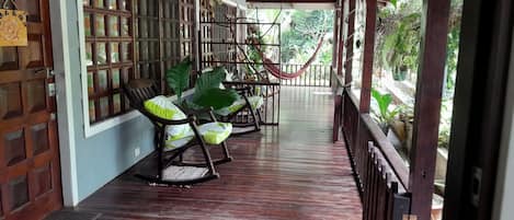 Eine hölzerne Veranda mit Schaukelstühlen und einer Hängematte, mit Blick auf einen Garten.
