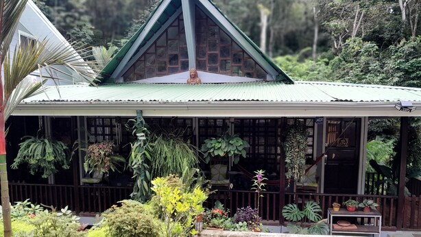 A house with a green roof, a covered porch, and various potted plants. - Casas Guaney (Quepos)