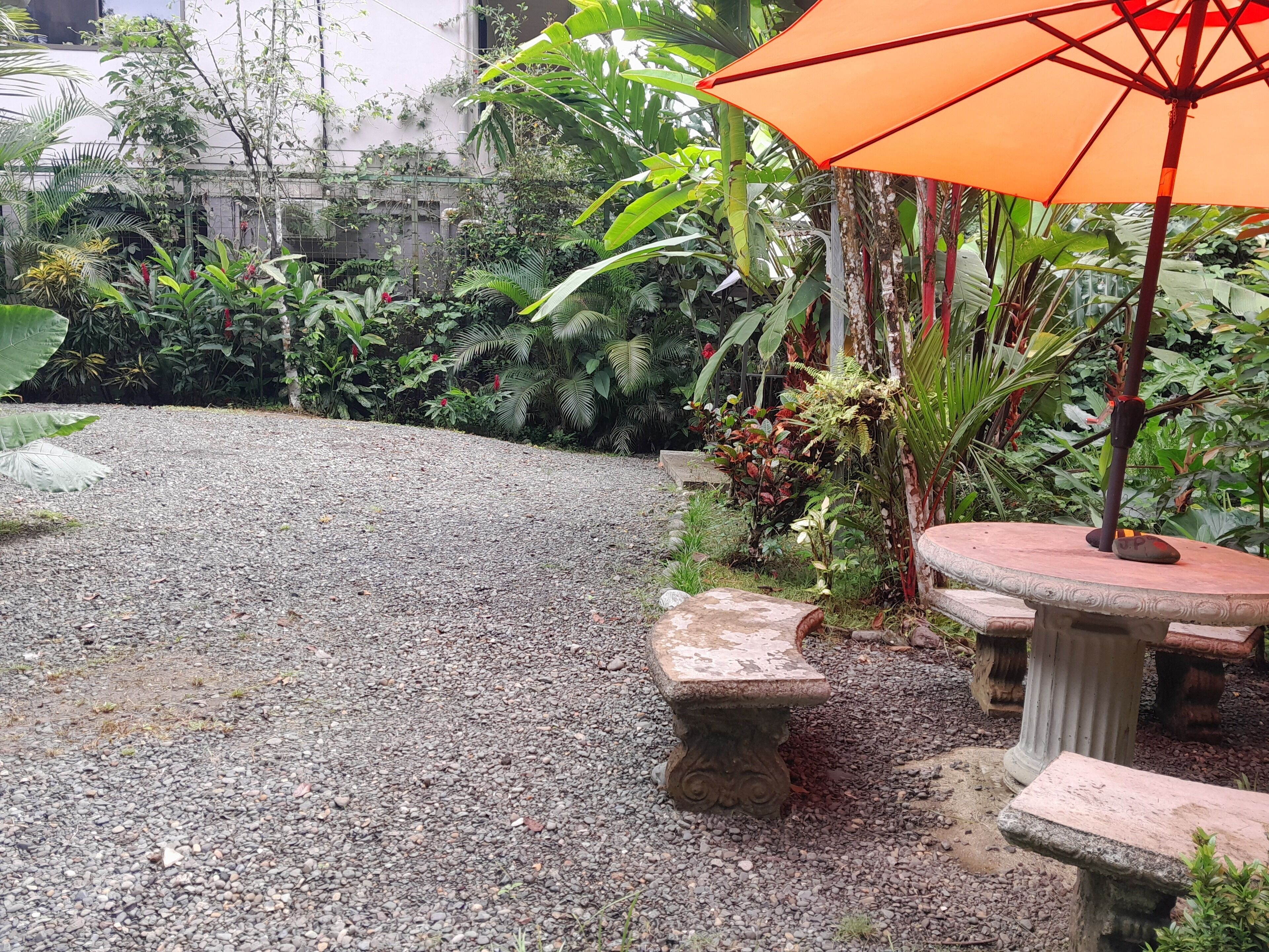 A gravel courtyard with a stone bench and an orange umbrella.
