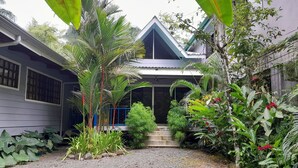 A house with a gravel driveway, surrounded by tropical plants and a blue railing. - Casas Guaney (Quepos)