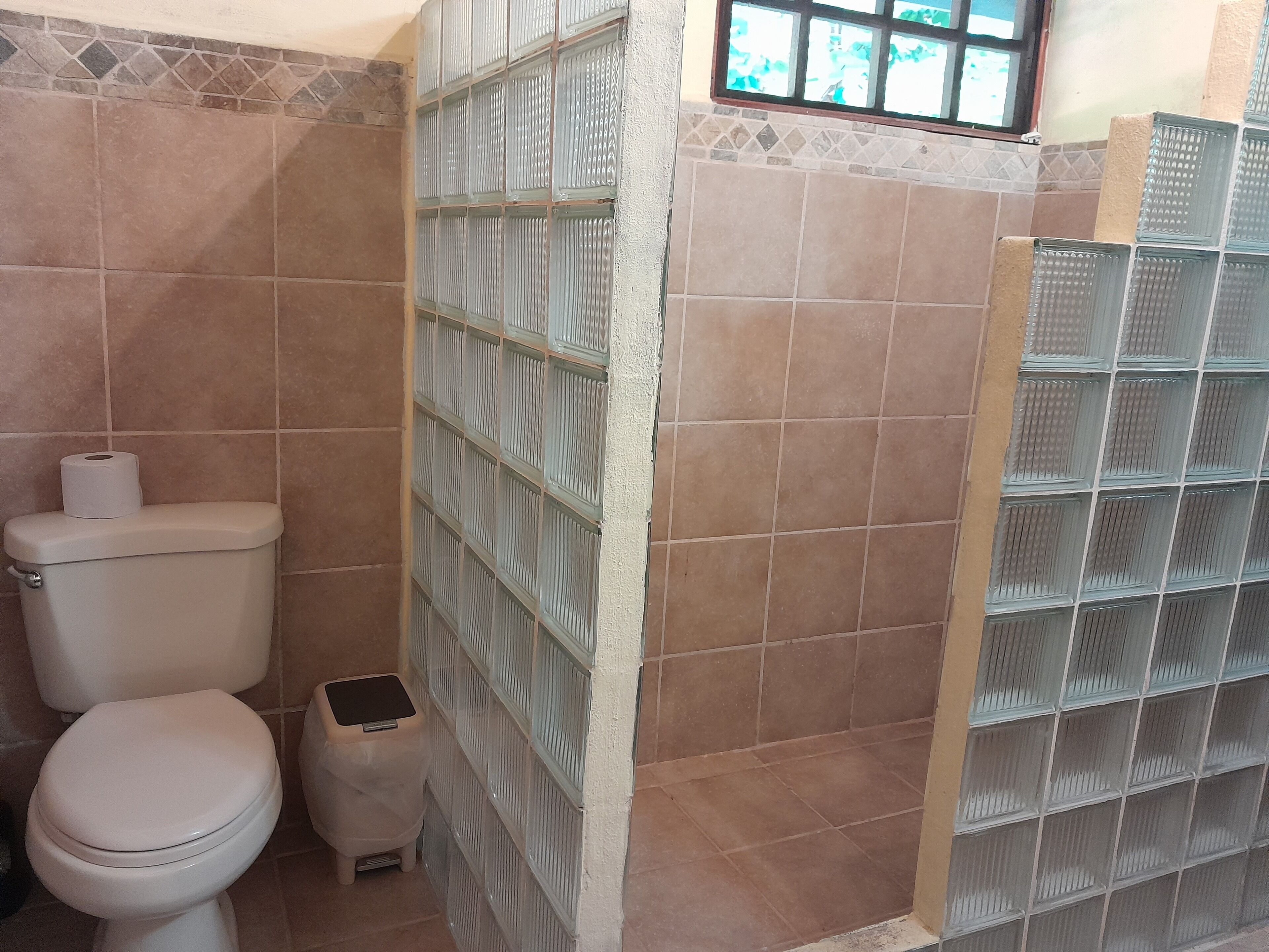 A bathroom with a toilet, a trash bin, and a window with a view.