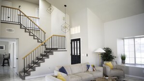 A spacious living room with a staircase, a sofa set, a coffee table, and a potted plant.