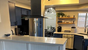 A modern kitchen with a central island, bar stools, stainless steel appliances, and a dining area with a table and chairs.