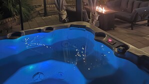 A hot tub with a blue light, surrounded by a covered patio area with string lights.
