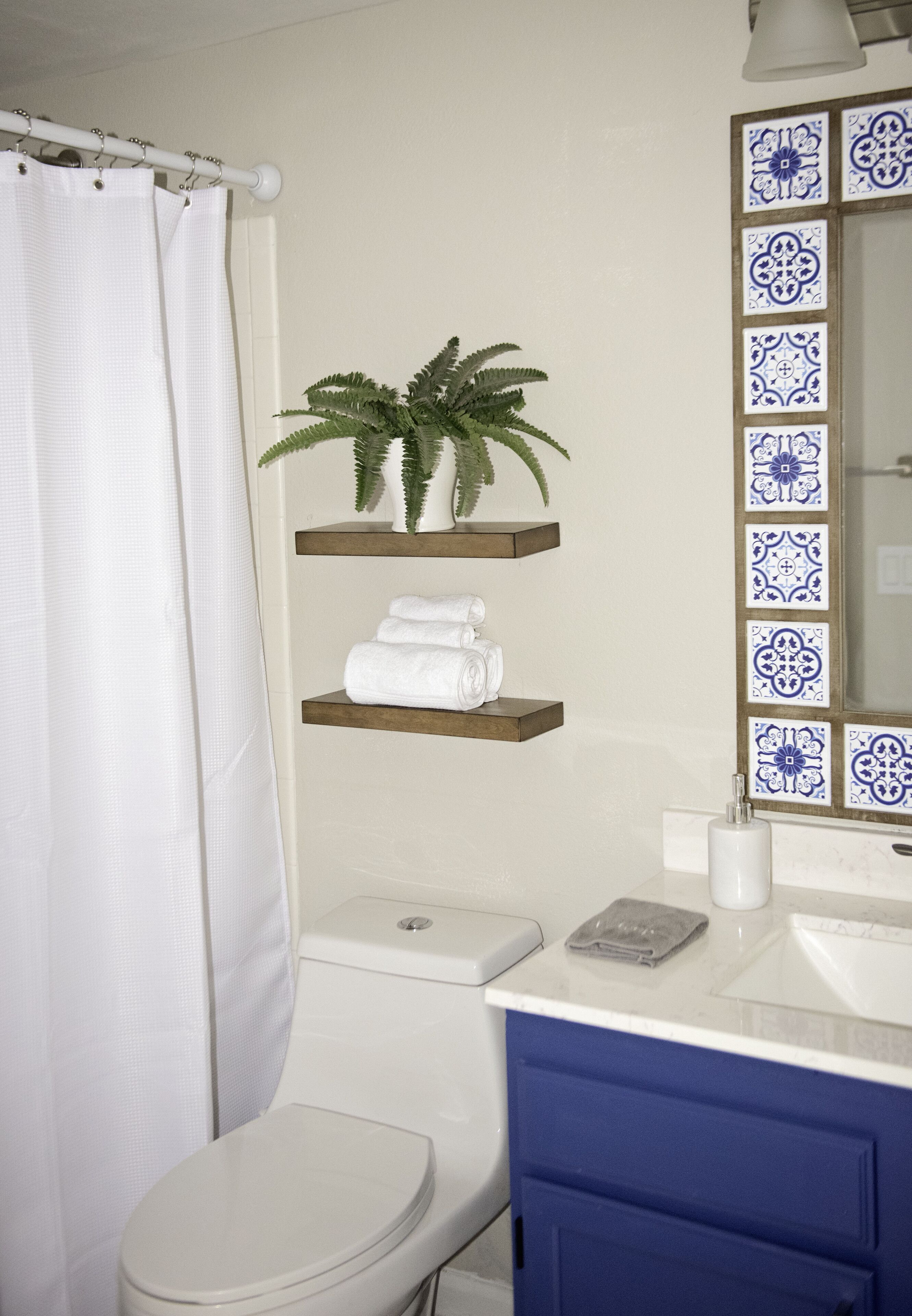 Un baño con un inodoro blanco, un mueble azul, un lavabo blanco, un espejo con azulejos azules y una cortina de ducha.
