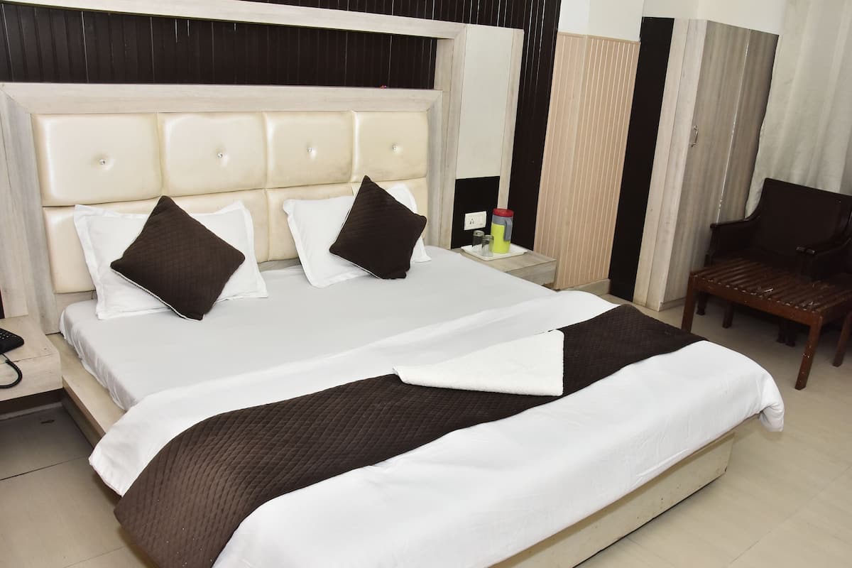 Quarto de hotel com uma cama grande, uma mesa de cabeceira de madeira, uma cadeira e uma mesinha de apoio com abajur.
