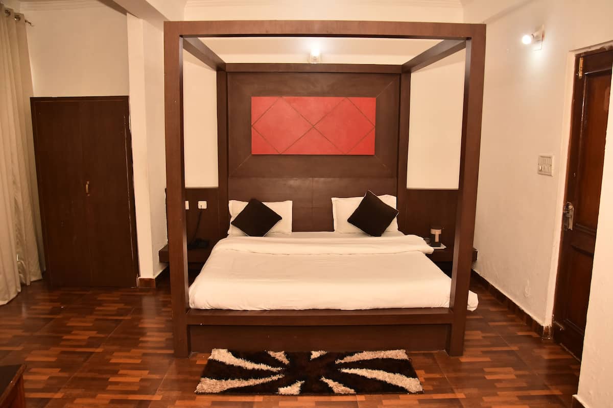 Uma cama de dossel com uma parede de destaque vermelha, piso de madeira e uma mesinha de cabeceira com luminária.