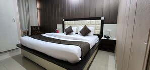 A neatly made bed with a white and brown bedspread, a tufted headboard, and two pillows. A red mug is on the nightstand beside the bed. - Hotel Neelkanth Mahadev Hotel & Resorts (Reasi)