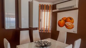 Un'area pranzo con tavolo e sedie bianche, una ciotola decorativa e un quadro con arance sulla parete.